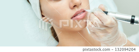 Young caucasian female receiving lip tattooing in beauty clinic by professional Young caucasian female receiving lip tattooing in beauty clinic by professional 132094204