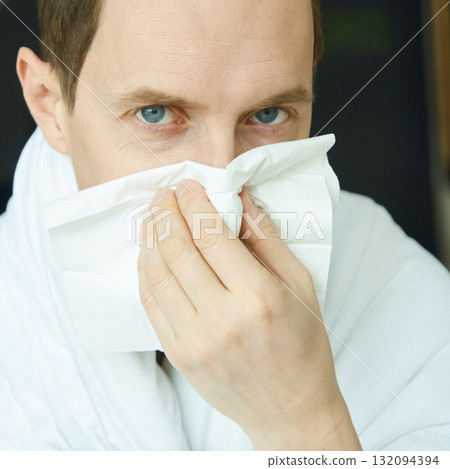 Caucasian adult male blowing nose in tissue feeling unwell indoors Caucasian adult male blowing nose in tissue feeling unwell indoors 132094394