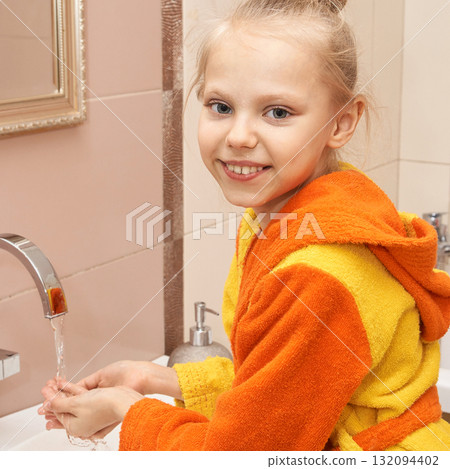 Smiling caucasian young girl in bright bathrobe washing hands in modern 132094402