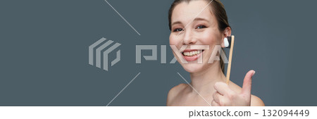 Caucasian female adult smiling holding eco-friendly bamboo toothbrush against 132094449