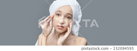 Young caucasian female applying eye patch with towel wrapped hair against gray Young caucasian female applying eye patch with towel wrapped hair against gray 132094593