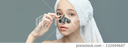 Young caucasian female applying charcoal nose strip with towel on head 132094687