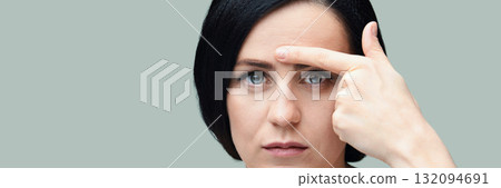 Caucasian young female with black hair pointing to forehead wrinkle on pale 132094691