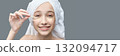 Young caucasian female applying eye patches smiling in towel headwrap on gray 132094717