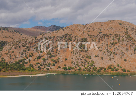 Drying mountain lake with wide strip of dried shore and orange rocky slope. Drying mountain lake with wide strip of dried shore and orange rocky slope. 132094767
