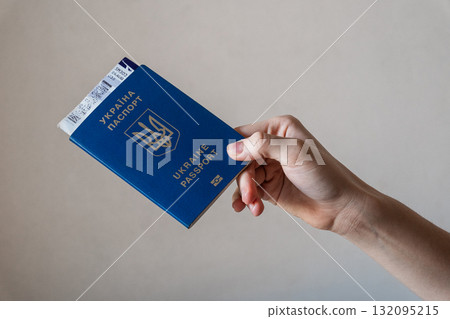 A hand holding a blue Ukrainian passport. The passport features the national emblem and text in Ukrainian and English. The background is neutral and simple. A hand holding a blue Ukrainian passport. The passport features the national emblem and text in Ukrainian and English. The background is neutral and simple. 132095215