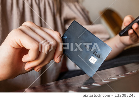 A young Caucasian woman holds a smartphone in one hand and a credit card in the other. She is engaged in online shopping or payment activity. A young Caucasian woman holds a smartphone in one hand and a credit card in the other. She is engaged in online shopping or payment activity. 132095245