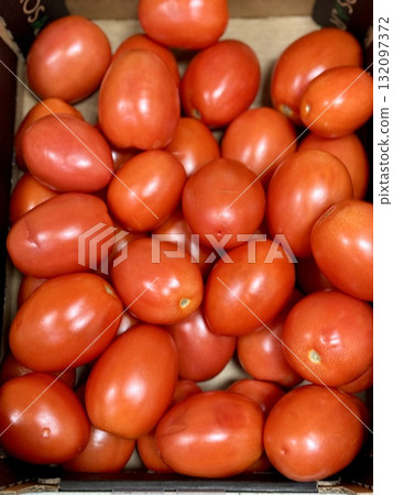 A vibrant display of ripe cherry tomatoes stacked neatly in a green basket at a bustling local market. Close-up. 132097372