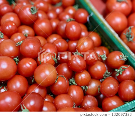 A vibrant display of ripe cherry tomatoes stacked neatly in a green basket at a bustling local market. Close-up. 132097383