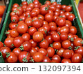 A vibrant display of ripe cherry tomatoes stacked neatly in a green basket at a bustling local market. Close-up. 132097394