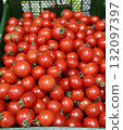 A vibrant display of ripe cherry tomatoes stacked neatly in a green basket at a bustling local market. Close-up. 132097397