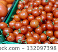 A vibrant display of ripe cherry tomatoes stacked neatly in a green basket at a bustling local market. Close-up. 132097398