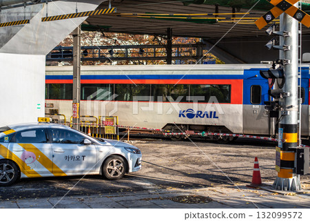 A Korail train passing under a bridge with a Kakao T taxi waiting at a crossing, city traffic in Seoul, South Korea A Korail train passing under a bridge with a Kakao T taxi waiting at a crossing, city traffic in Seoul, South Korea 132099572