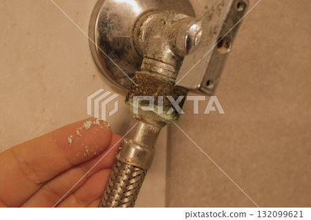Female hand on an old, oxidized water faucet with hose: moisture damage and limescale Female hand on an old, oxidized water faucet with hose: moisture damage and limescale 132099621