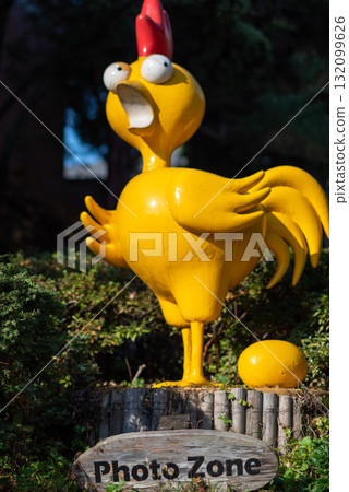 Photo zone sign with a whimsical yellow chicken statue in a garden 132099626