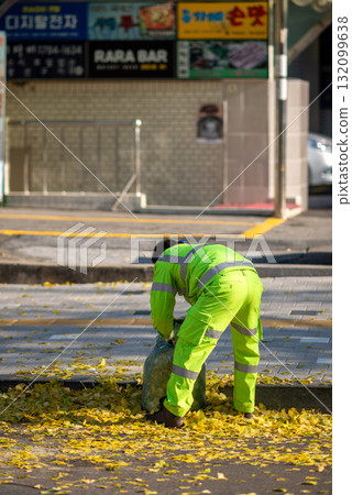 A worker in bright green uniform gathering fallen yellow leaves on a sidewalk in Seoul, South Korea A worker in bright green uniform gathering fallen yellow leaves on a sidewalk in Seoul, South Korea 132099638