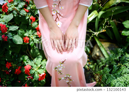 Portrait of Asian girls with Ao-Dai Vietnam traditional dress costume  sitting in flower garden 132100143