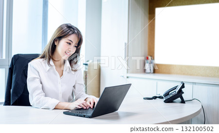 Happy attractive asian business woman smiling working with laptop in modern office 132100502