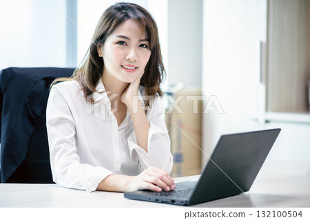 Happy attractive asian business woman smiling working with laptop in modern office 132100504