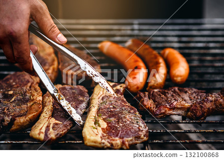 chef grilling steaks  with grilled sausages barbecue on flaming 132100868