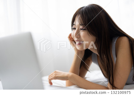A young woman operating a computer in bed 132100975