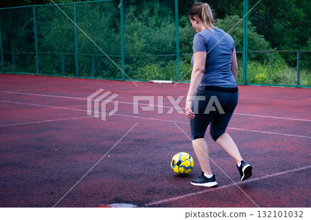 Woman playing soccer on a red court. She kicks a yellow ball, enjoying outdoor exercise. Woman playing soccer on a red court. She kicks a yellow ball, enjoying outdoor exercise. 132101032
