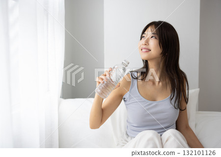 Young woman drinking bottled water in bed Young woman drinking bottled water in bed 132101126