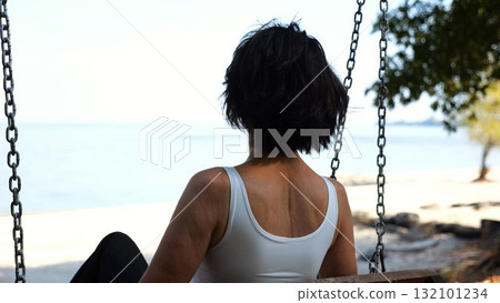 Happy woman ride on swing at tropical at sea beach. Carefree lady enjoying rest near ocean. Adult female having fun at sea shore on sunny day. Concept of summer vacation or holiday. Slow motion 132101234