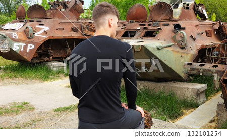 Young man looking at destroyed military equipment of the russian army. Exhibition of rusty and burned-out armored vehicles on ukrainian territory. War between Ukraine and russia. Slow motion 132101254