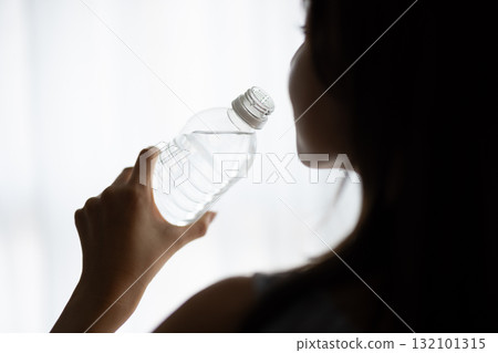 Rear view of a young woman drinking bottled water by the window 132101315