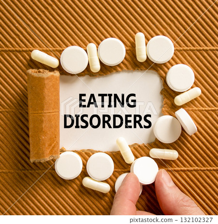 Eating disorders symbol. Concept words Eating disorders on beautiful white paper. White pills tablets. Doctor's hand. Beautiful brown background. Medical healthy lifestyle eating disorders concept. 132102327