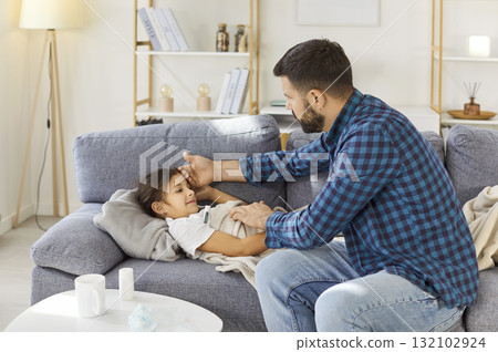 Father caring for sick child at home, checking fever and offering comfort 132102924