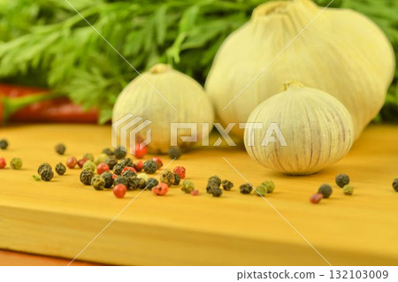 A bulb of garlic, red chili peppers, four-color pepper, and carrot tops on a wooden cutting board. The concept of cooking and vegetables in the home. Macro image, close-up. Garlic - Allium sativum is A bulb of garlic, red chili peppers, four-color pepper, and carrot tops on a wooden cutting board. The concept of cooking and vegetables in the home. Macro image, close-up. Garlic - Allium sativum is 132103009