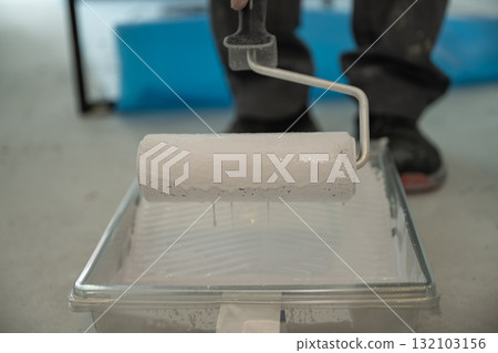 Close-up of a roller soaked in white paint on a ribbed plastic tray. Concept for renovation, paint preparation, and DIY interior renovation. Close-up of a roller soaked in white paint on a ribbed plastic tray. Concept for renovation, paint preparation, and DIY interior renovation. 132103156