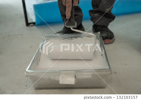 Close-up of a roller soaked in white paint on a ribbed plastic tray. Concept for renovation, paint preparation, and DIY interior renovation. 132103157