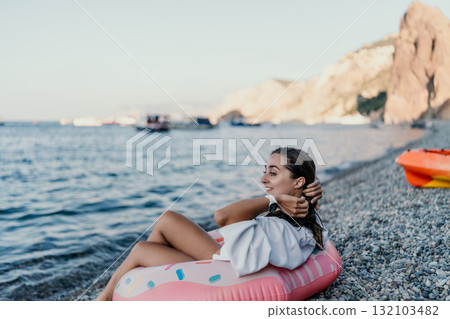 Woman, beach, vacation. Happy woman relaxes on an inflatable donut on a pebble beach enjoying summer. 132103482