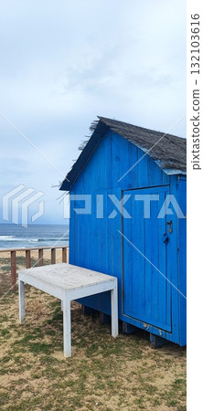 Closed at the end of the season, this coastal beach bar features white tables, palm tree decor, and a surfboard-shaped sign by the ocean. 132103616