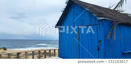 Closed at the end of the season, this coastal beach bar features white tables, palm tree decor, and a surfboard-shaped sign by the ocean. 132103617