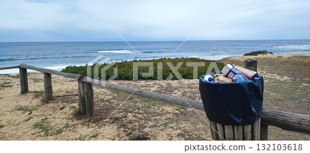An eco-friendly wooden trash bin located along a coastal path overlooking the sea. A concept of sustainability, environmental awareness, and coastal landscape preservation. 132103618