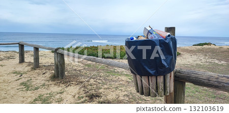 An eco-friendly wooden trash bin located along a coastal path overlooking the sea. A concept of sustainability, environmental awareness, and coastal landscape preservation. 132103619