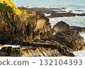 The shot captures a rugged coastline along the South Ring, Ireland. Rocky cliffs meet the Atlantic Ocean, with waves crashing against the shore in bright daylight. 132104393