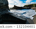 On a sunny day, waves from the ocean gently wash up on the black sand beach at Sheep Cove in Ireland, among the rocks and cliffs. 132104401