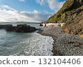 Rocky Irish coastline. Waves meet the pebbled beach beneath a grassy cliff. 132104406