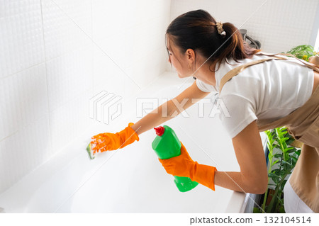 Woman in rubber gloves and apron manually washes bathtub is in bathroom of house with sponge cleaner and cleaning agent in a bottle. Restoring order, cleanliness and hygiene in home, cleaning servise Woman in rubber gloves and apron manually washes bathtub is in bathroom of house with sponge cleaner and cleaning agent in a bottle. Restoring order, cleanliness and hygiene in home, cleaning servise 132104514