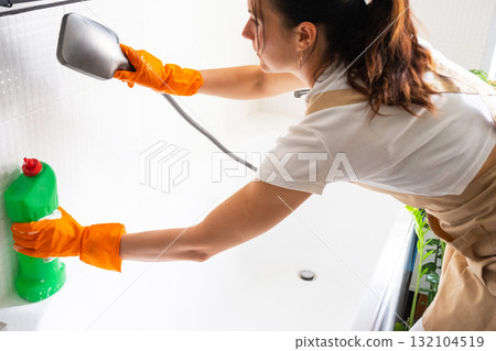 Woman in rubber gloves and apron manually washes bathtub is in bathroom of house with sponge cleaner and cleaning agent in a bottle. Restoring order, cleanliness and hygiene in home, cleaning servise Woman in rubber gloves and apron manually washes bathtub is in bathroom of house with sponge cleaner and cleaning agent in a bottle. Restoring order, cleanliness and hygiene in home, cleaning servise 132104519