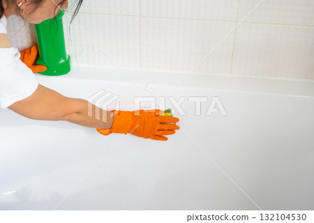 Hands in rubber gloves close-up and bottle of detergent is in bathroom of house with sponge cleaner and cleaning agent on bath. Restoring order, cleanliness and hygiene in home, cleaning servise 132104530