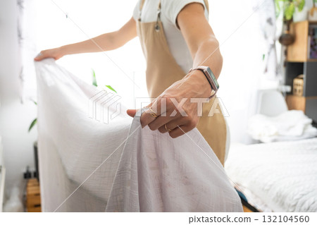 A housewife woman in an apron irons linen curtains in a room on an ironing board A housewife woman in an apron irons linen curtains in a room on an ironing board 132104560