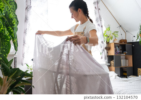 A housewife woman in an apron irons linen curtains in a room on an ironing board A housewife woman in an apron irons linen curtains in a room on an ironing board 132104570