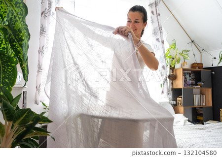 A housewife woman in an apron irons linen curtains in a room on an ironing board A housewife woman in an apron irons linen curtains in a room on an ironing board 132104580
