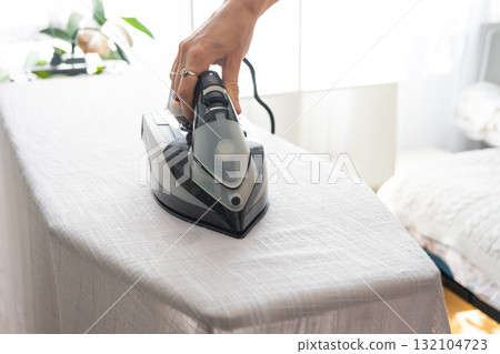 Close up hand housewife woman in an apron irons linen curtains in a room on an ironing board 132104723